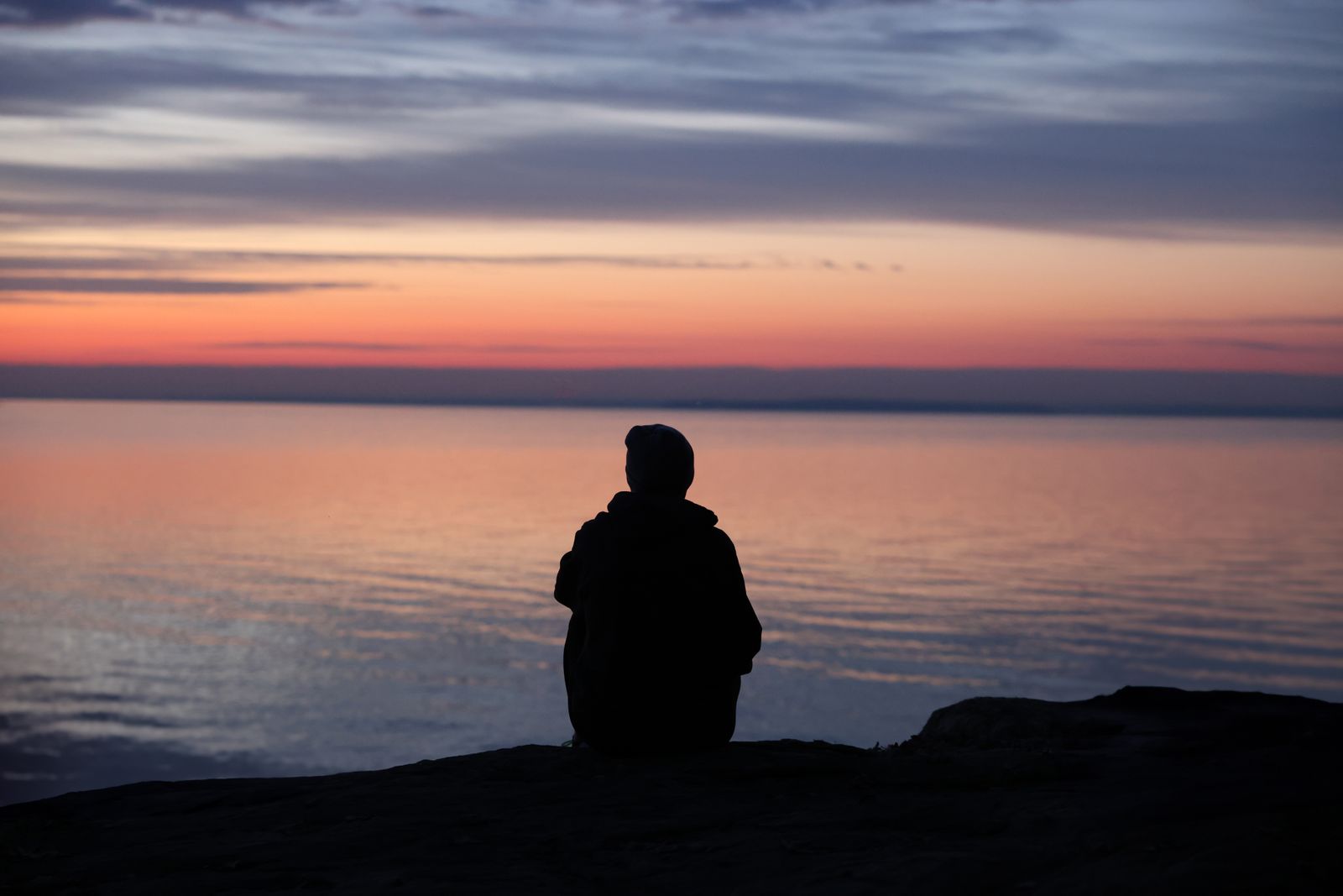 Silhouette of a Person Sitting at a Seashore and Enjoying a Sunset ...