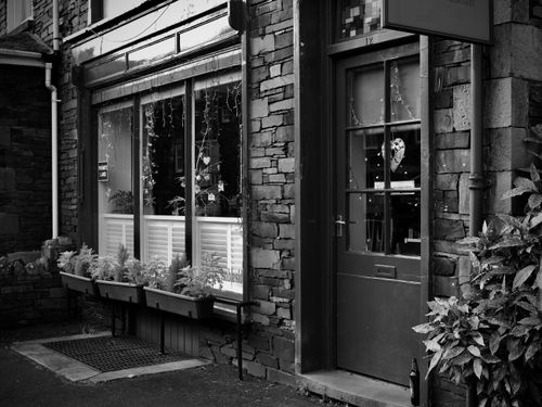 Free A quaint café entrance with potted plants and rustic facade in black and white. Stock Photo