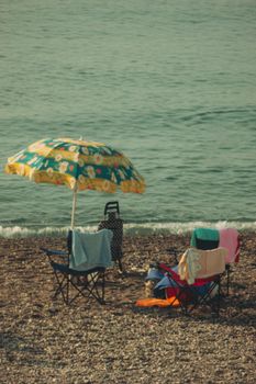 Relaxing beach scene with chairs and umbrella on a pebble shore.
