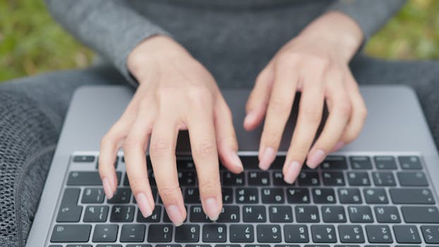 Hands typing on a laptop keyboard in an outdoor setting, capturing a modern, portable work environment.