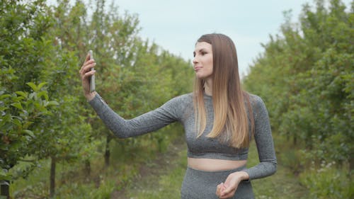 A modern sports woman takes pictures on the nature smartphone, recording a video blog. Sports video vlog. Video Blog athlete. Girl blogger points to the camera nature.
