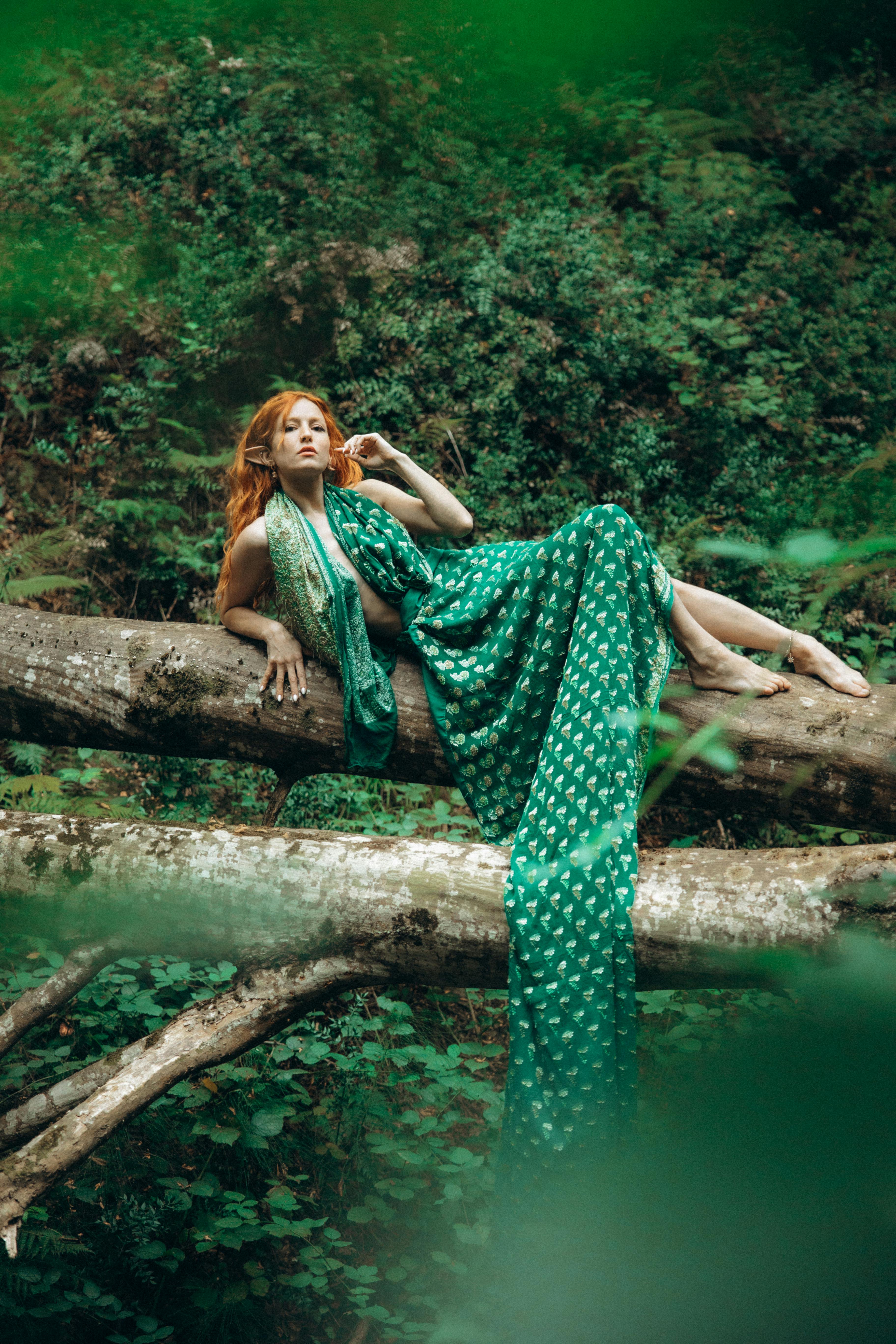 a woman in a green dress laying on a tree branch