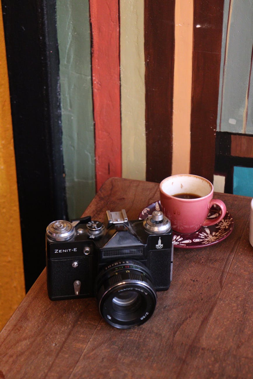 A vintage Zenit camera beside a cup of coffee on a wooden table.
