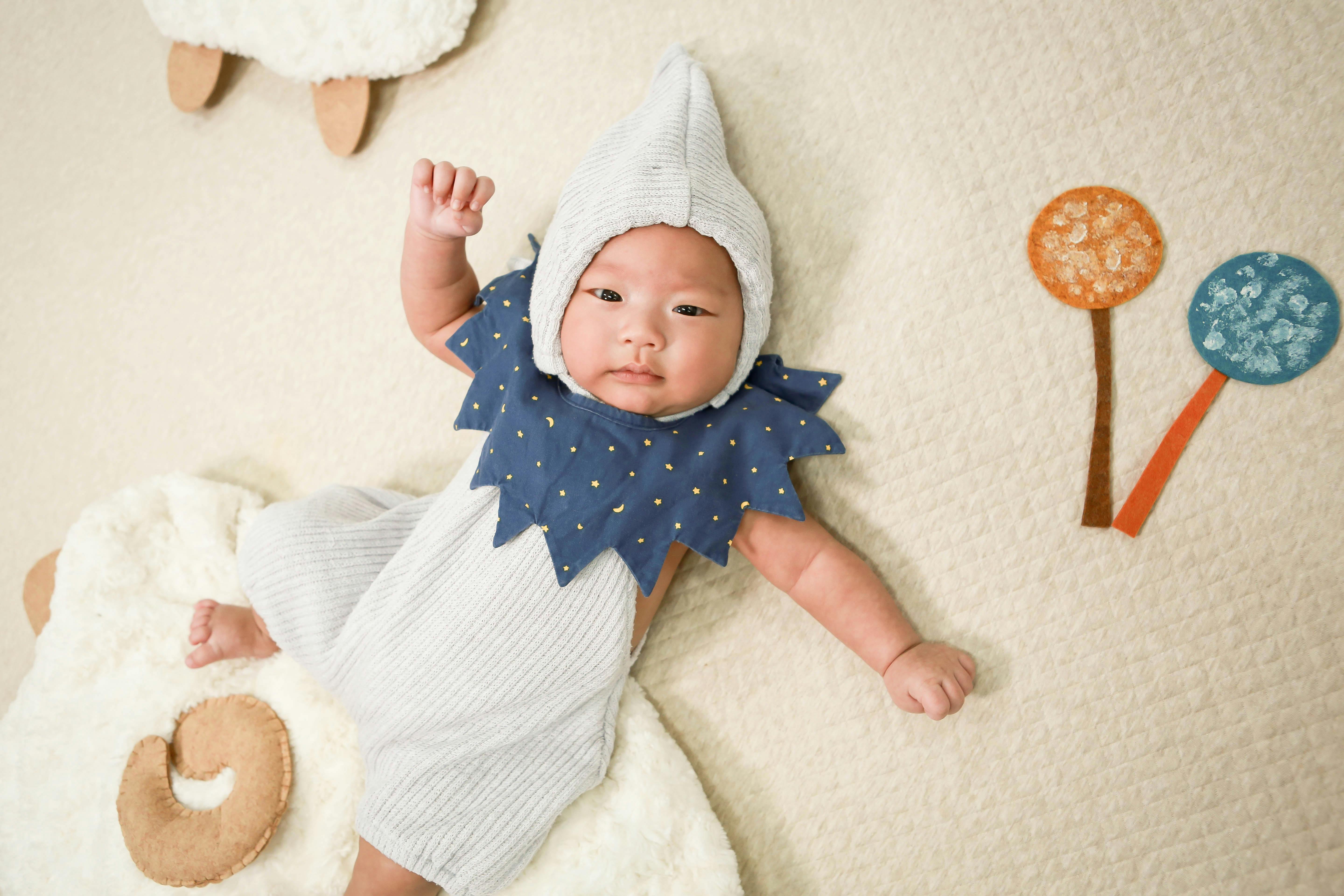 Cute baby in a creative hat and outfit lying on a soft surface with whimsical decorations.