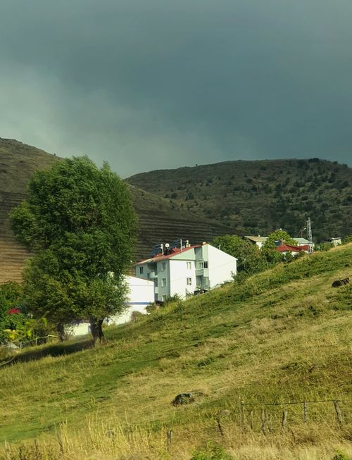 Free Serene rural view with houses, hills, and trees under a cloudy sky. Stock Photo