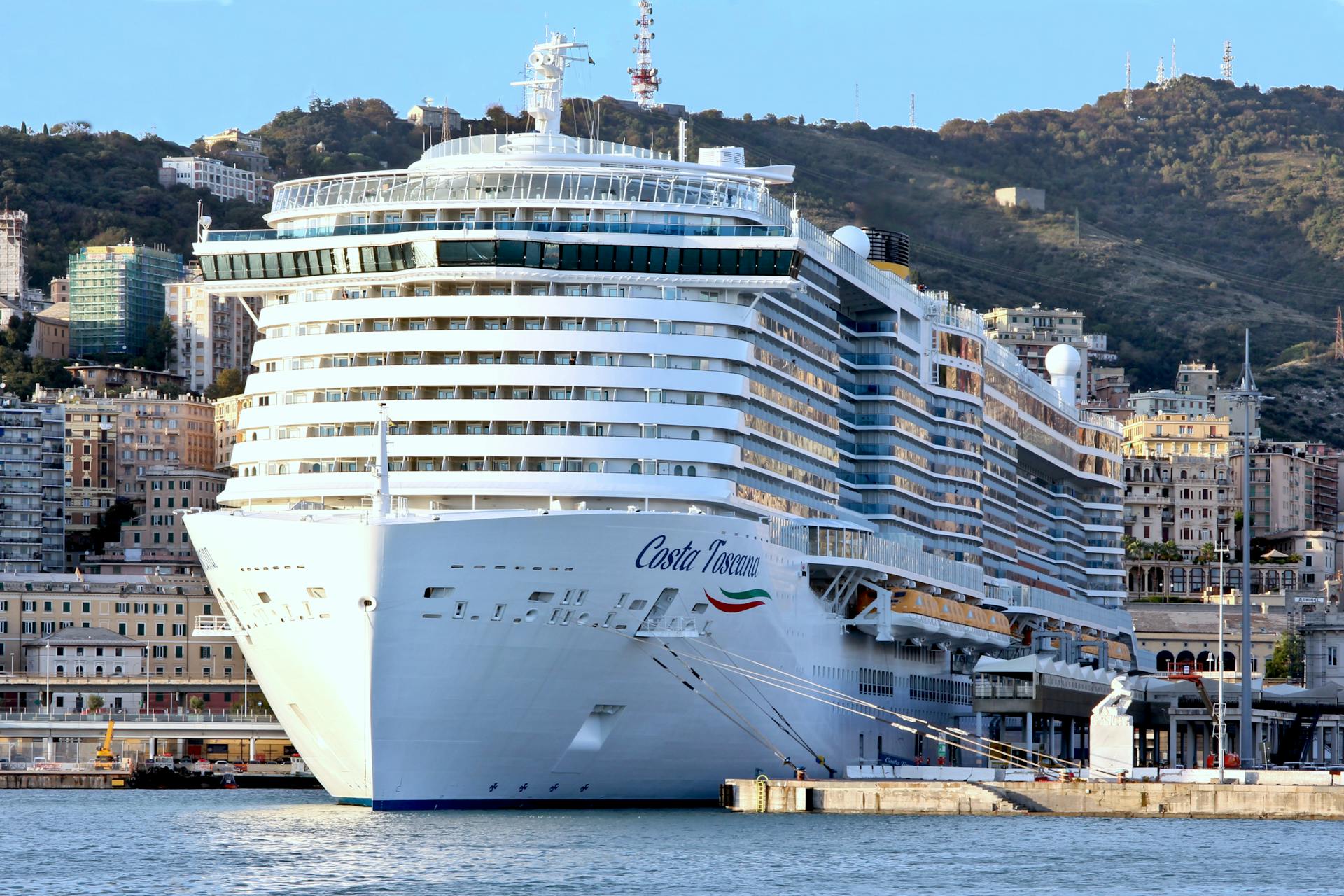 Elegant Costa Toscana cruise ship docked in a picturesque urban harbor with hillside backdrop.