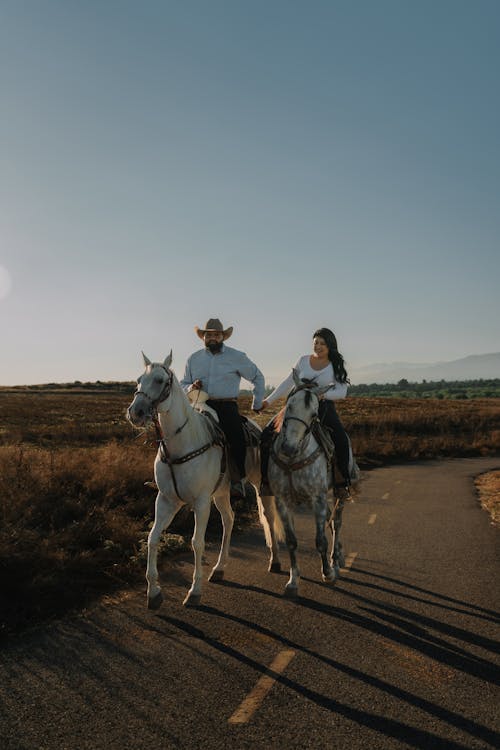 Happy Couple Riding Horses Down Road Holding Hands 