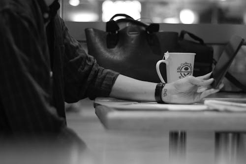 Gray Scale Photograph of Person Sitting Beside Black Leather Bag