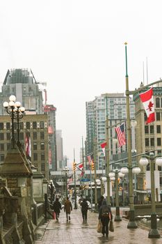 People walking on a rainy city street lined with flags and buildings.