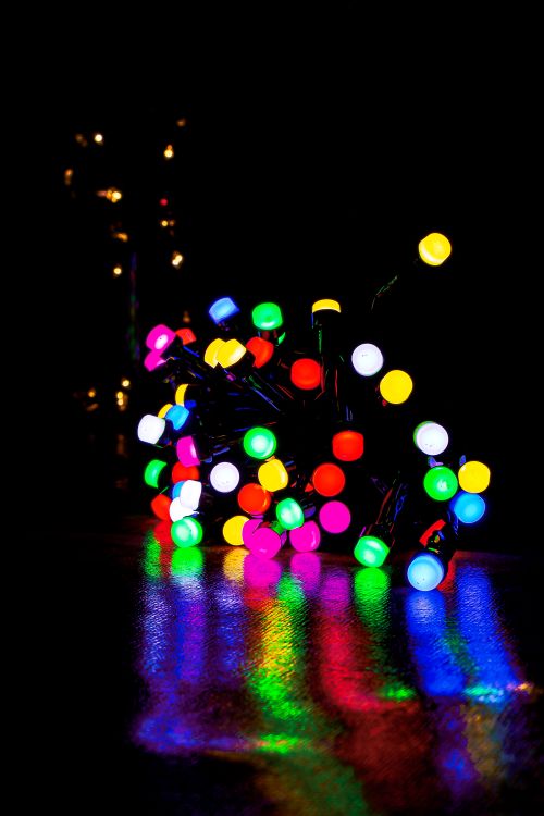 Free Colorful Christmas lights reflecting on a dark surface, creating a festive atmosphere. Stock Photo