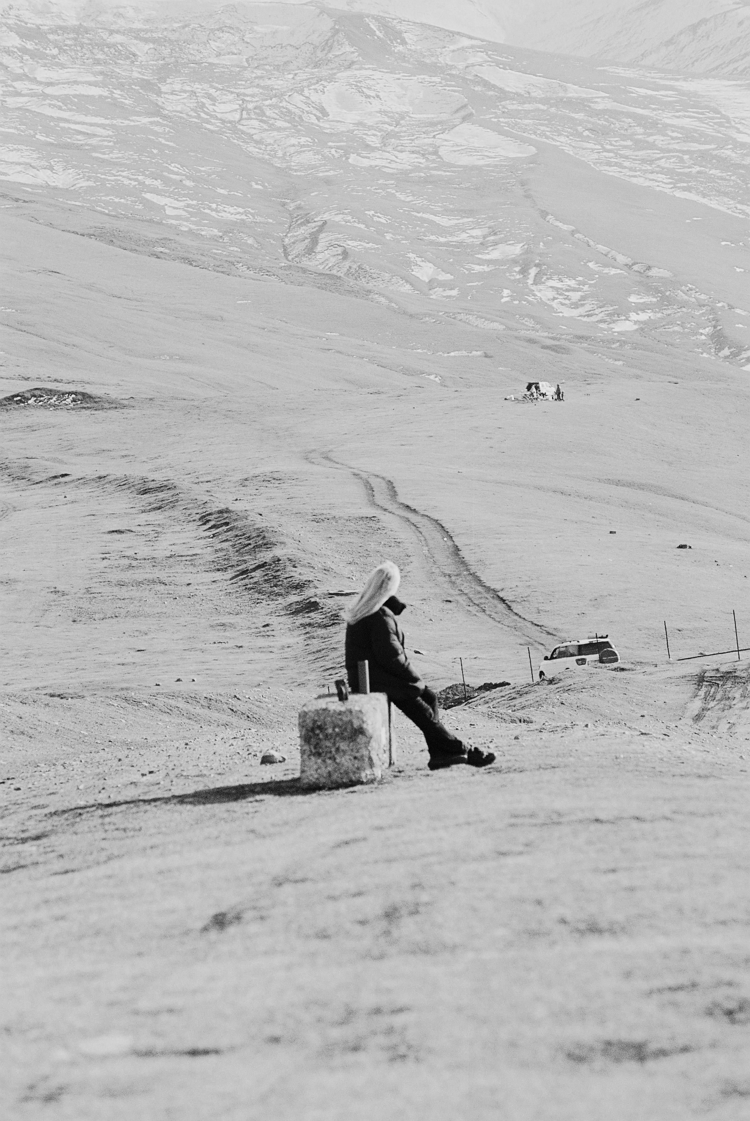 A solitary figure sitting in a vast, barren Kazakhstani landscape captured in black and white.