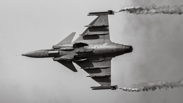 Black and white image of a military fighter jet in flight with smoke trails, showcasing aviation prowess.