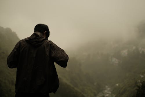 Man in Jacket Standing by Valley on Foggy Day