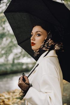 Stylish woman with umbrella and headscarf posing outdoors, reflecting classic elegance.