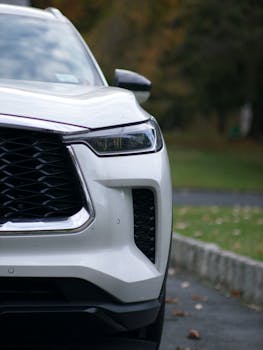 Close-up shot of a luxury white SUV featuring its grille and headlight on a road.