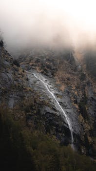 A tranquil waterfall cascading down a rocky cliff in misty mountains of Ginzling, Tirol, Austria.