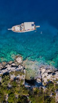 Aerial view of a boat floating on the clear turquoise waters off the rocky coast of Antalya, Türkiye. Perfect travel destination.
