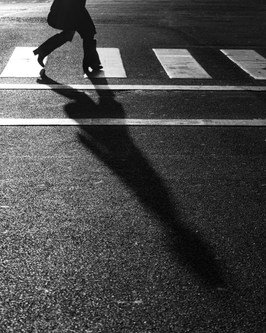 Black and white photo of a person crossing a street in Buenos Aires with dramatic shadows.