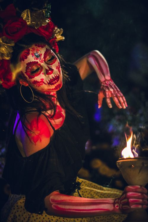 Free A woman celebrates Dia de Muertos with a traditional painted face holding a candle at night. Stock Photo