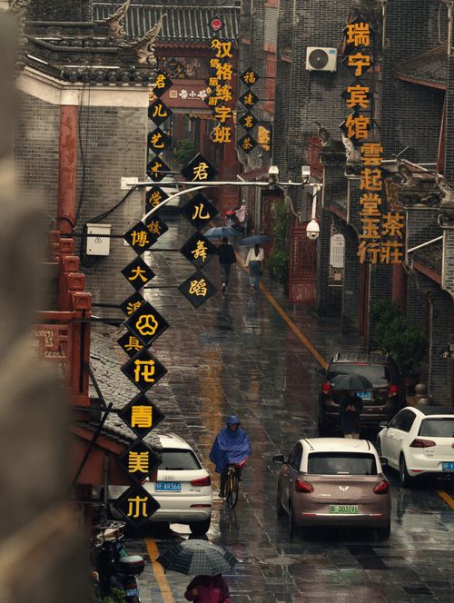 Free A rainy street in an urban Asian city with a cyclist and cars amidst traditional architecture. Stock Photo