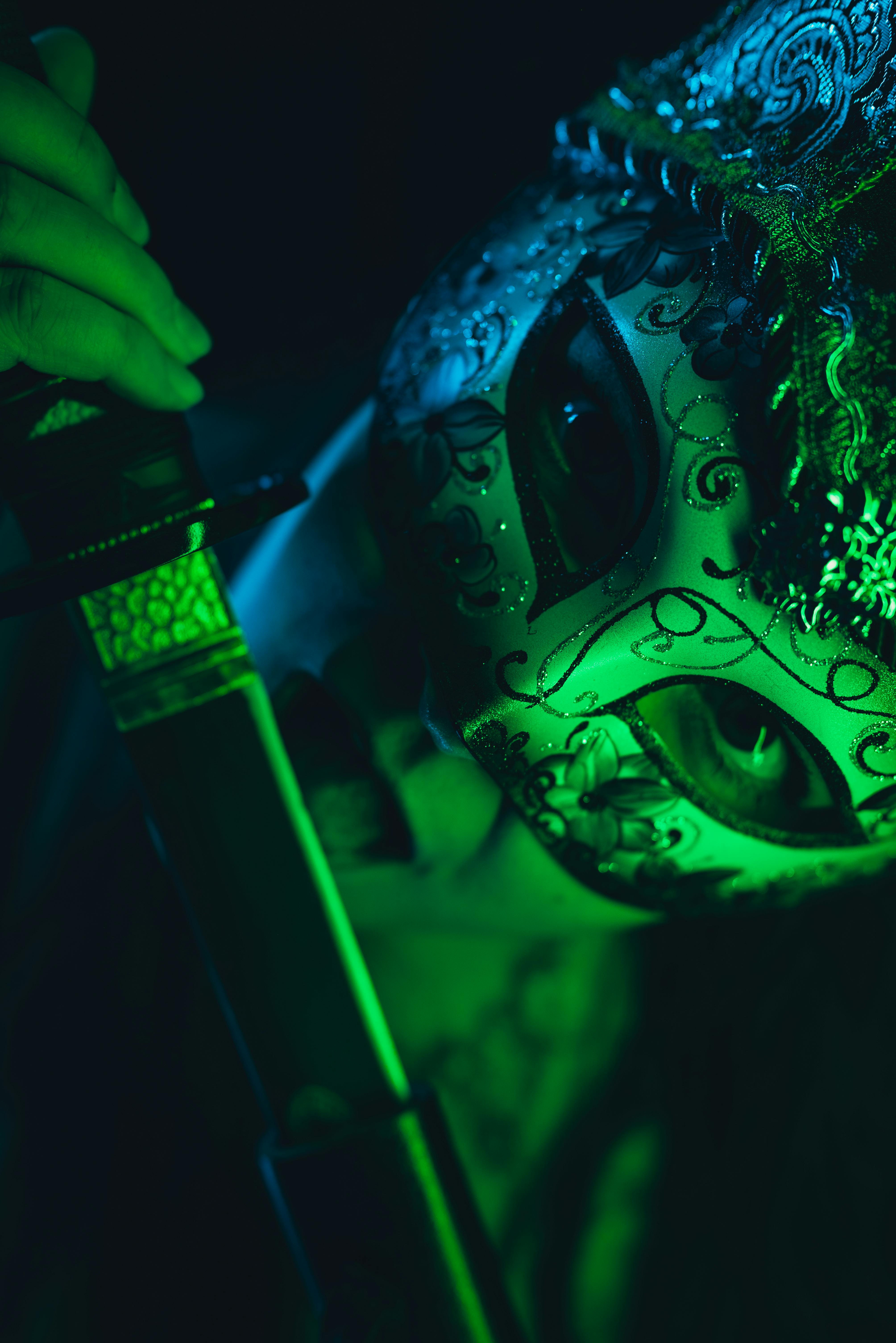 Intriguing photo of a person in a mask with ornate details and a sword, under green lighting.