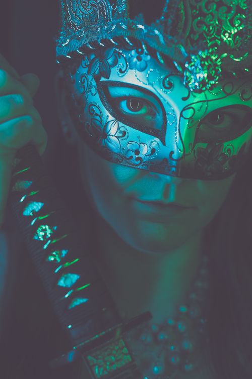 Free A woman in an ornate mask holding a sword, captured in moody blue-green lighting. Stock Photo
