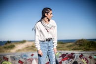 沿海滑板公园里，一位扎着辫子、穿着牛仔裤和运动衫的年轻女子