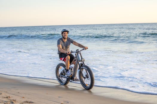 Smiling man riding an electric bike by the ocean on a sunny day.