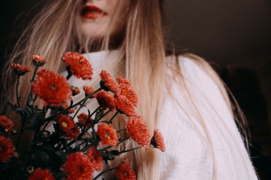 Artistic portrait of a woman holding bright red flowers indoors.