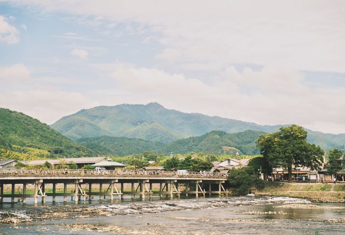 Discover the serene landscape of Arashiyama with its picturesque bridge and lush green mountains in Kyoto, Japan.