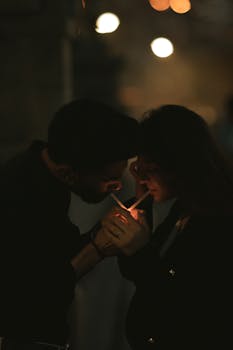 Young couple smoking together in a dimly lit outdoor night scene, sharing a lighter.