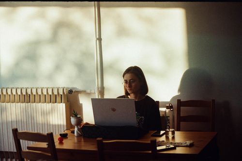 Free A woman concentrates on her laptop in a warmly lit dining room, capturing a calm work environment. Stock Photo