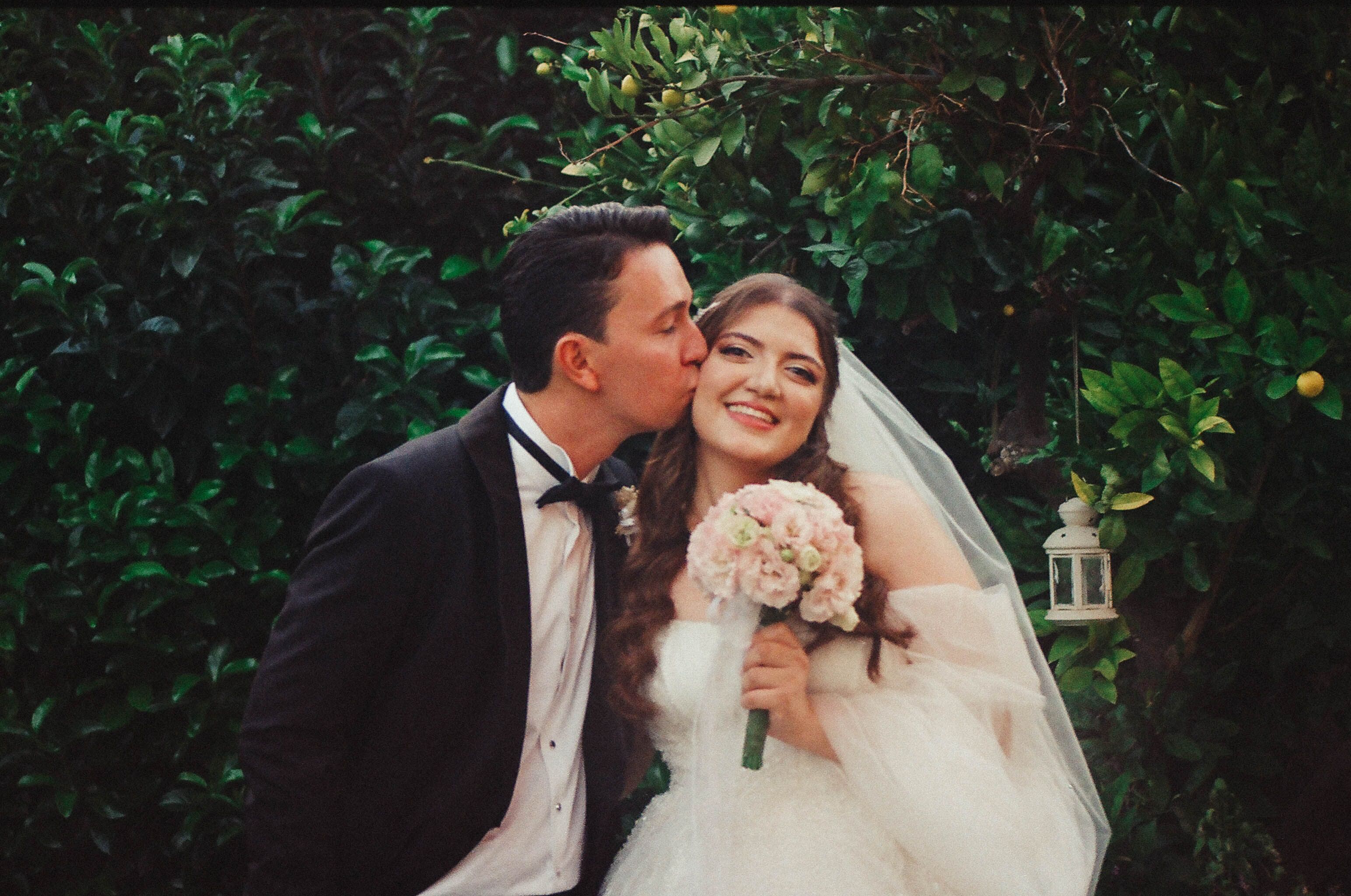 Smiling bride and groom embrace in a lush outdoor garden, capturing a tender wedding moment.