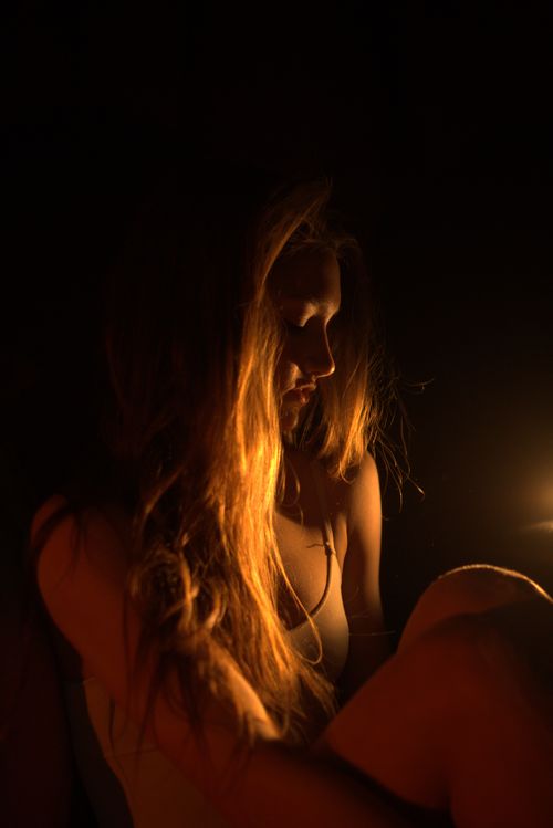 Free A woman with long hair illuminated by candlelight, creating a moody atmosphere. Stock Photo