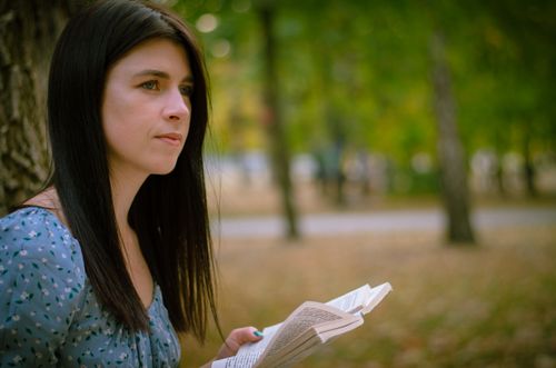 Free A thoughtful woman with dark hair reads a book while sitting in a park during fall. Stock Photo