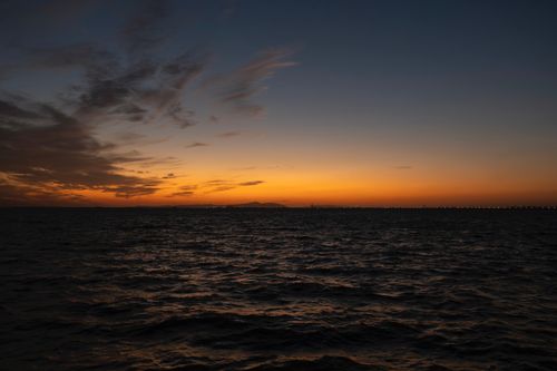Free A tranquil sunset with vibrant colors over a calm sea, featuring a distant bridge silhouette. Stock Photo