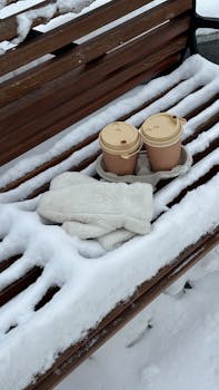 Warm knit gloves and coffee cups on a snow-covered bench in winter in Novokuznetsk, Russia.