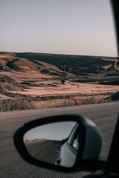 A scenic rural landscape reflected in a car mirror during a road trip.