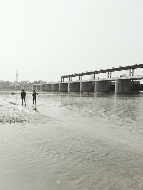 Free Grayscale scene of two people by a river and a bridge, serene atmosphere. Stock Photo