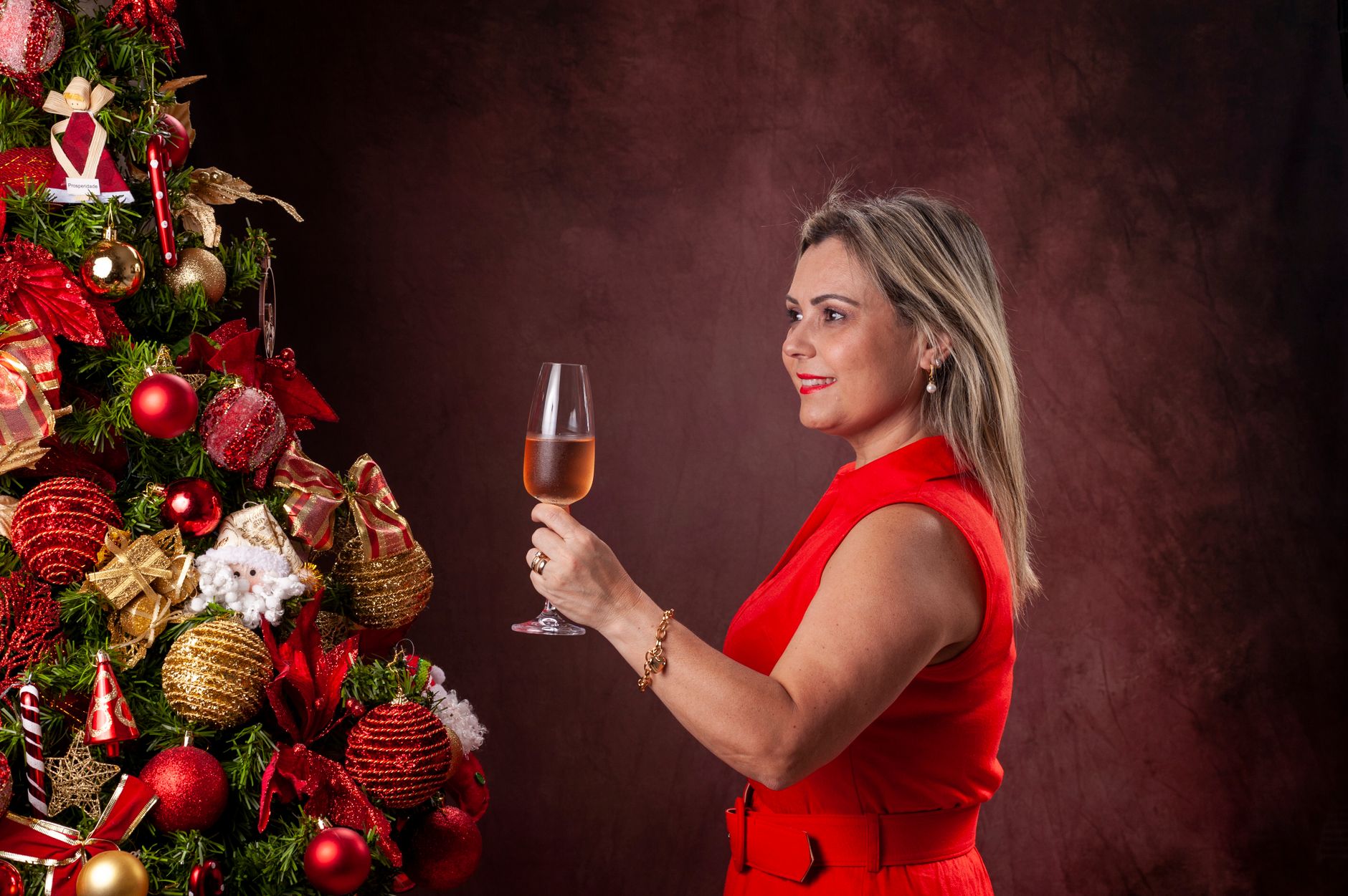 Woman in red dress enjoying rosé beside a decorated Christmas tree.