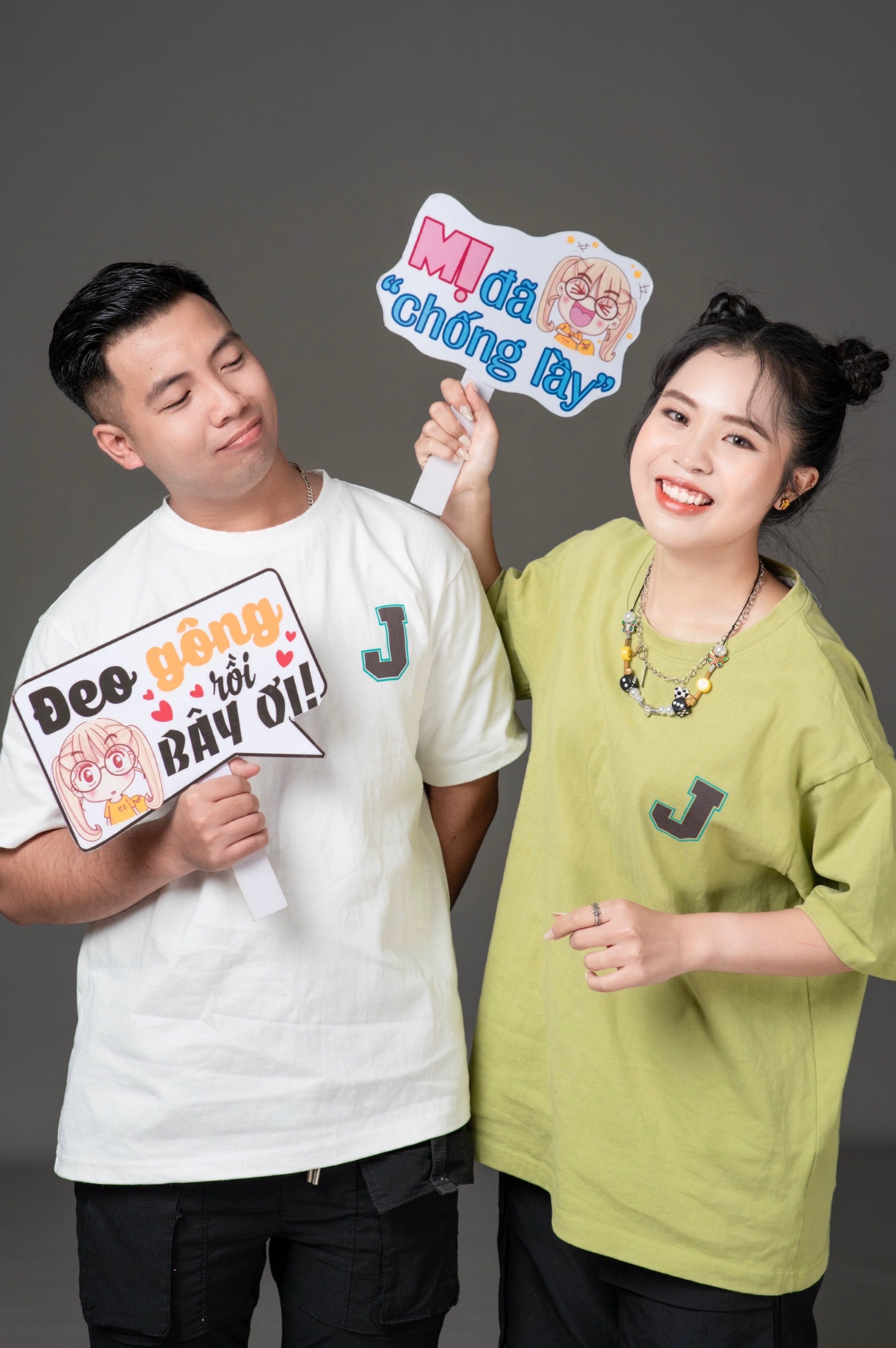 A cheerful couple posing with playful signs in a studio setting, expressing joy and humor.
