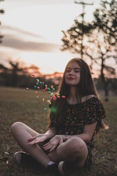 日落时分，一位年轻女子坐在户外，投掷着色彩缤纷的软糖豆，捕捉下这无忧无虑的时刻