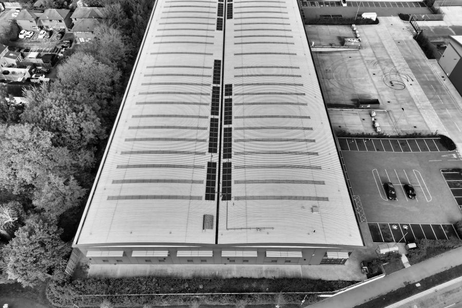 Black and white aerial view of a warehouse in Hertfordshire with solar panels and parking area.