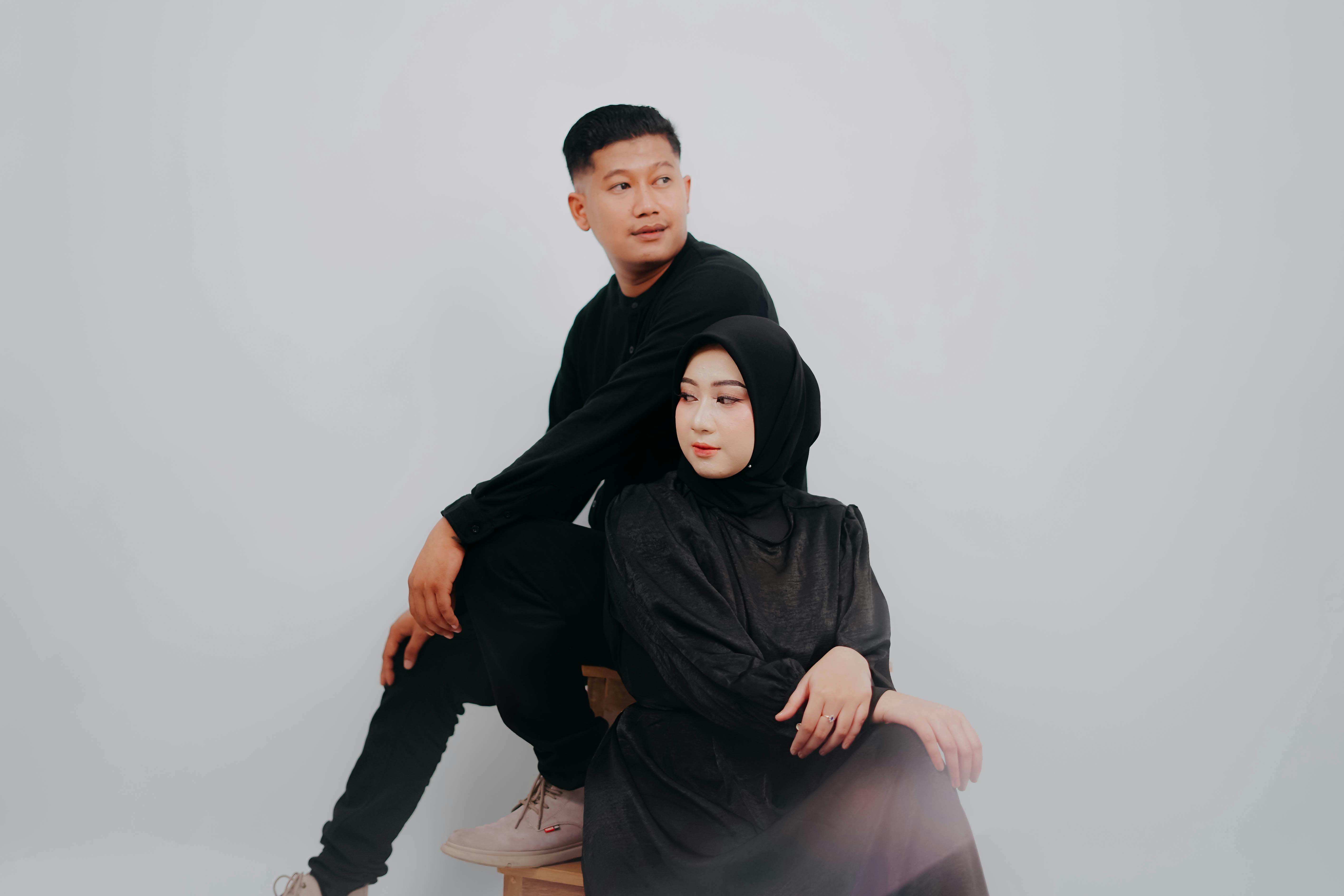 Stylish couple in black attire posing elegantly in a studio with a white background.