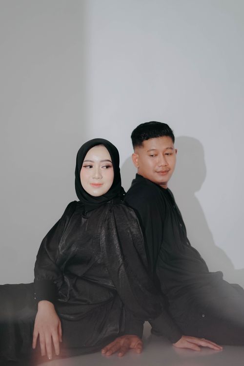 Free Fashionable studio portrait showcasing a man and woman both wearing black outfits, seated back-to-back. Stock Photo