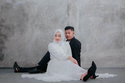 A stylish couple poses elegantly in a modern wedding photo shoot against a gray backdrop.
