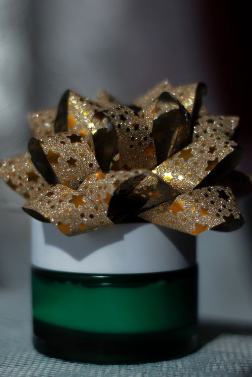 Free Close-up of a glittering golden gift bow on a green cylinder, ideal for festive celebrations. Stock Photo