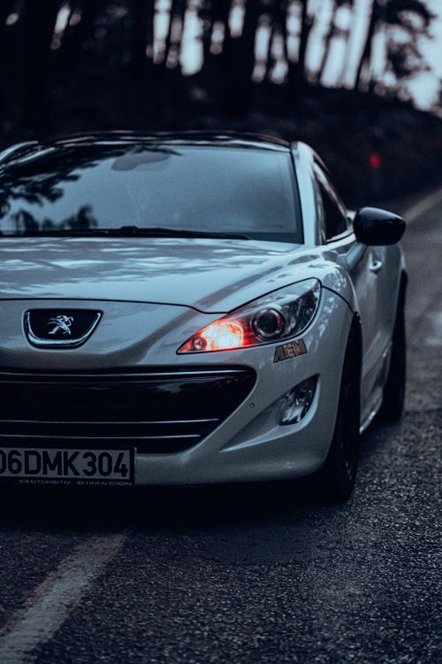 Free Close-up of a white sports car, Peugeot RCZ, on a wet road at dawn, adding elegance and speed. Stock Photo