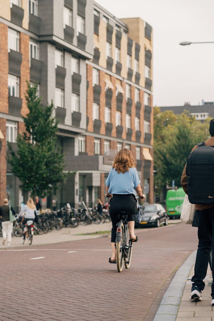 Back View Of A Woman On A Bicycle On A Sidewalk In City 