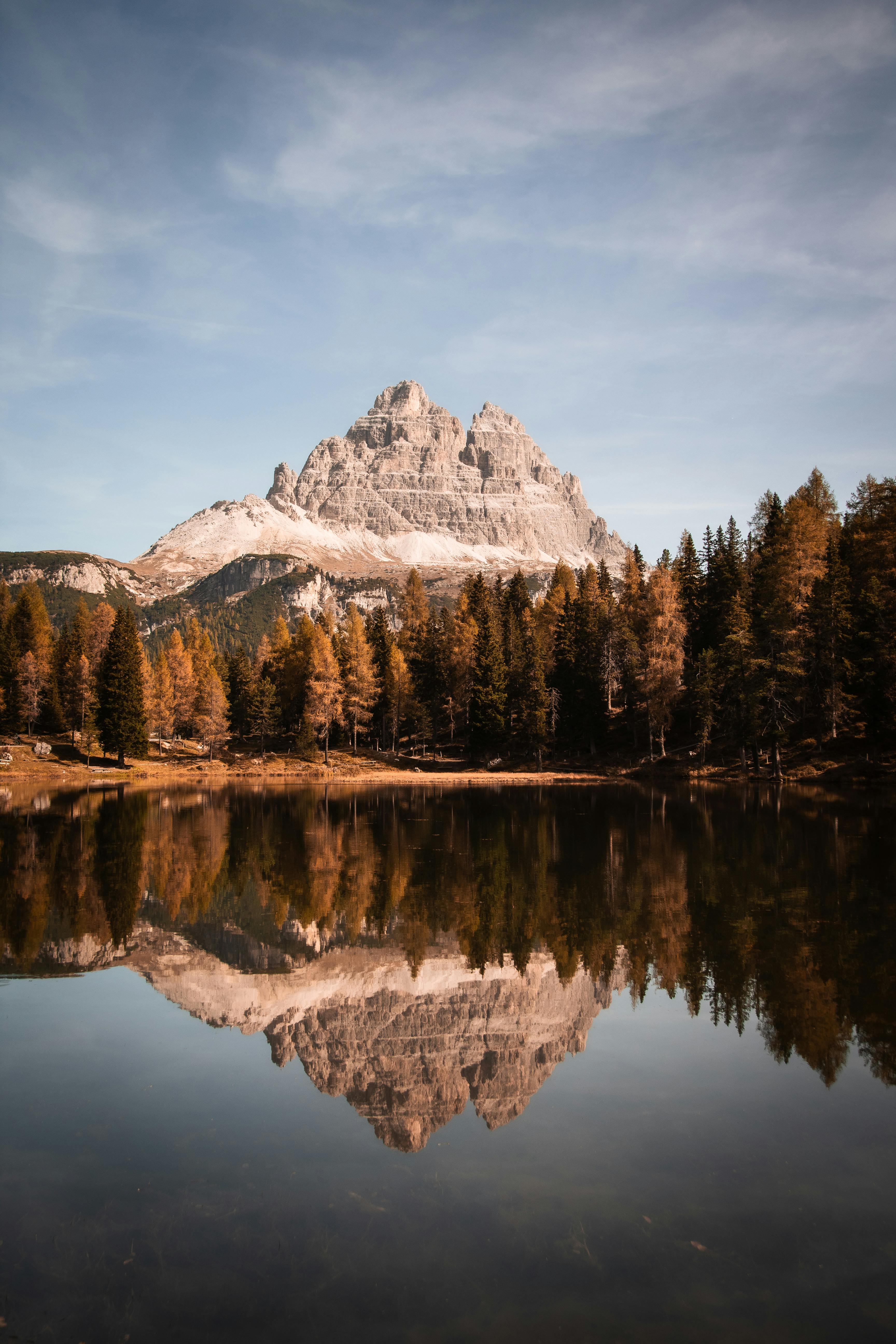 Peaceful scene of Italian Alps reflected in a serene lake surrounded by a lush forest.
